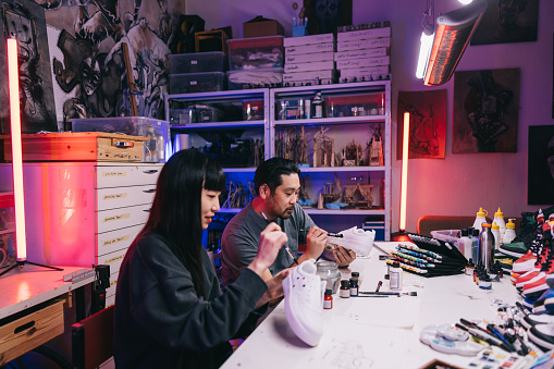 In a bustling studio filled with vibrant energy, two passionate Japanese sneaker artists 
collaborate on a new project, fueled by their shared love of innovative design.