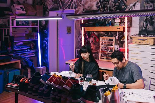 In a bustling studio filled with vibrant energy, two passionate Japanese sneaker artists 
collaborate on a new project, fueled by their shared love of innovative design.