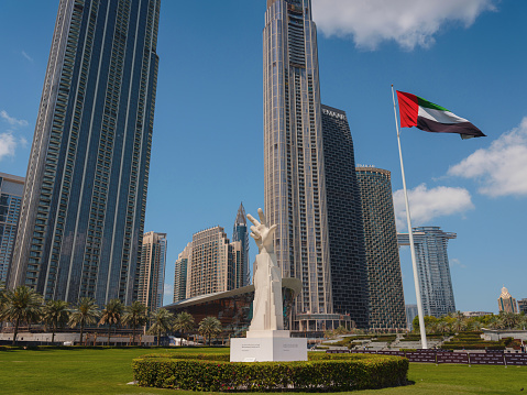 20 March 2023, Dubai, UAE: three fingers statue near UAE flag in sunny day and Burj Khalifa known as tallest skyscraper in world, United Arab Emirates. It is known for being world's tallest building.