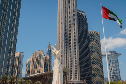 20 March 2023, Dubai, UAE: three fingers statue near UAE flag in sunny day and Burj Khalifa known as tallest skyscraper in world, United Arab Emirates. It is known for being world's tallest building.