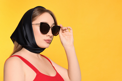 Young woman with lip piercing and sunglasses on yellow background, space for text