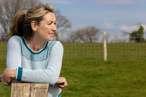 Attractive thoughtful middle aged woman leaning resting on a wooden fence post in the countryside or her garden