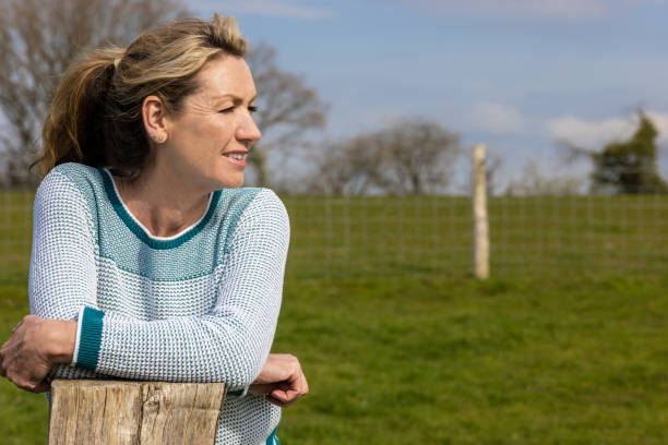 Attractive Thoughtful Middle Aged Woman Resting on Wooden Fence Post - fotografia de stock