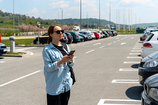 Woman using her mobile phone while standing on car parking.