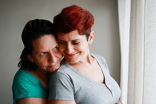 Gay senior lesbian couple hugging indoor at home - Diversity, LGBTQ lesbian family and love concept - Soft focus on right woman ear