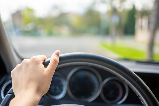 View of a woman's hand on the steering wheel of a car while driving in the city. High quality photo