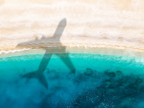 Vacation at tropical paradise near sea. Aerial view of beach and sea shore with airplane arriving at destination. Summer vacation background with place for text. Shoot directly above.