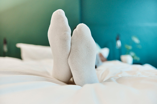 Sleeping, morning feet and bedroom man relax in home bed for health, wellness and tired after long day sleep. Foot, socks and male person sleep for fatigue, mental health and dream about relaxation