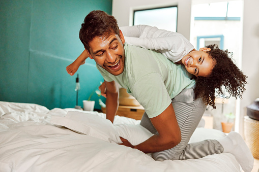 Family, laughing and father play with girl in bedroom for bonding, quality time and having fun in morning. Happy family, love and female child on bed to relax, playing and enjoy games with father