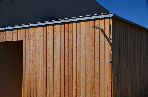 wooden paneling on the garden house from a metal container. screw the slats from rough prisms. it is a design element and a replacement for the facade in the garden, roof gutter, slate