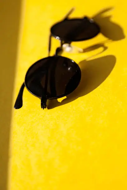 black sunglasses lying on the side in the sun on yellow background, seventies model