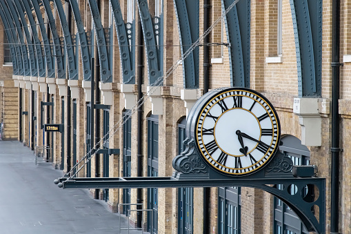 London, England-August 2022; View of the large analog clock on the platform of Kings Cross station with brick side of concourse and steel beams of the roof of the station