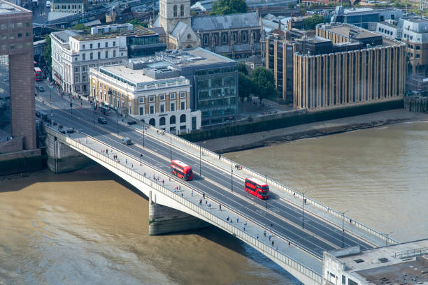 London, England-August 2022; High level view of two bright red double deck busses on London Bridge crossing the Thames river with view to the South Bank