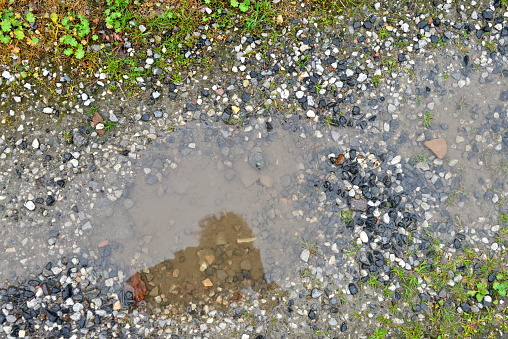 Reflection of a photographer who sees and shoots himself in a puddle on a gravel road with subsidence