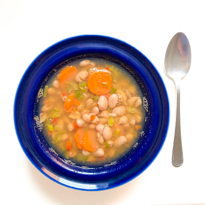 High angle view of delicious white bean soup with carrots ready to eat for lunch at home in the kitchen table . Also a plate with slices of wholemeal bread .