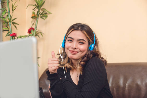 a portrait of a vlogger showing a thumbs up sign to show approval. she is wearing a blue wired headset. - filipino ethnicity audio imagens e fotografias de stock