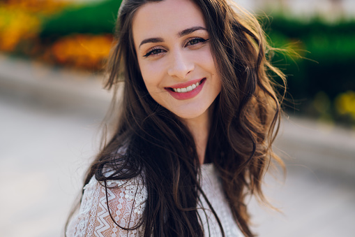 Beauty photo of a young trendy boho woman smiling at the camera on a sunny summer day outdoors. Headshot of a young brunette with a perfect smile.