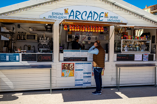 An outdoor food vendor located at the weekend flea market in Cannes, France.  A wide variety of food is offered to the hungry crowd at the market.