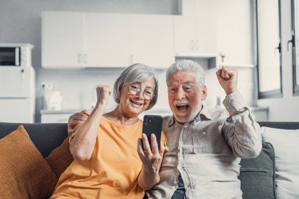 istock Happy older couple sit on couch staring at cellphone screen gesturing looking overjoyed, scream with joy, read fantastic news, get great commercial offer, pension raise. Success, achievement concept 1488875801