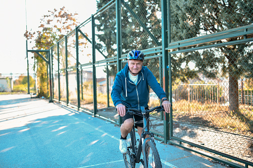 Smiling Senior Male Riding Bicycle On Court