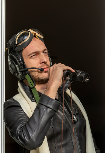 Portrait of young man in leather jacket, white scarf, leather helmet, glasses and flight headset