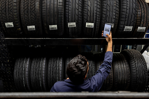 Latin American employee scanning a bar code on a tire at a garage shop using a cell phone