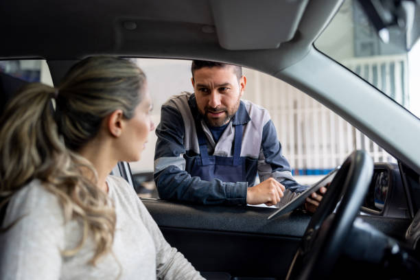 mecánico explicando a una mujer el diagnóstico en su coche después de una exploración - auto repair shop mechanic digital tablet customer fotografías e imágenes de stock