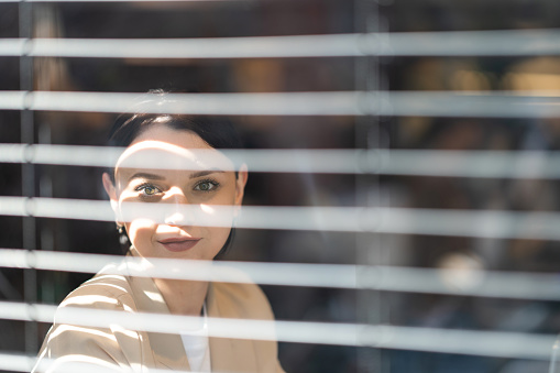 Young beautiful businesswoman looking out of the window through the blinds