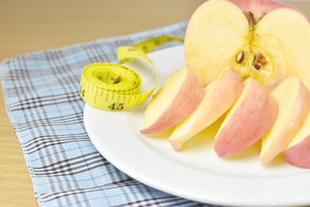 Diet concept, apple with measuring tape on wooden background.