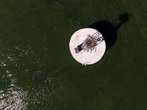 An aerial view of a circular concrete base with a solar-powered beacon and antenna in the middle of the waters of Oyster Bay on Long Island, NY