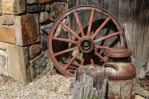 An antique wagon wheel, featuring wooden and metallic spokes, sits beside a vintage wall