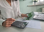 Woman is counting on calculator and writing with pen in notebook closeup