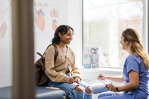 The young adult female patient smiles while listening to the nurse give an encouraging update regarding her medical exam that was recently completed.