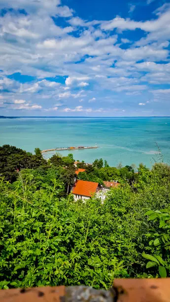 View to the clear blue water of the Lake Balaton with trees and sky with clouds. Sunny day of spring in Tihany, town of Hungary.