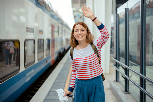 Tourist woman with backpack Waving her hand in a train station. Female tourist greeting and enjoy, travel concept. Theme transportation and travel.