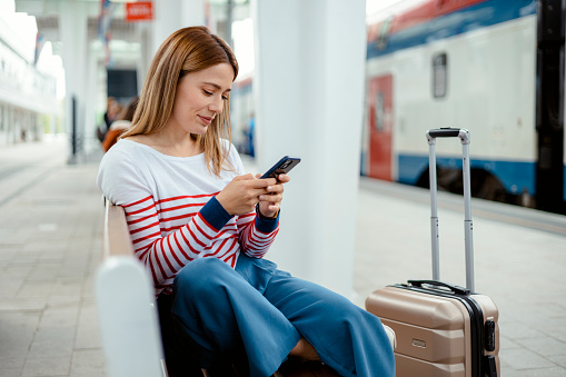 Female passenger texting on smartphone at train station. Travel and active lifestyle concept. Travel by train