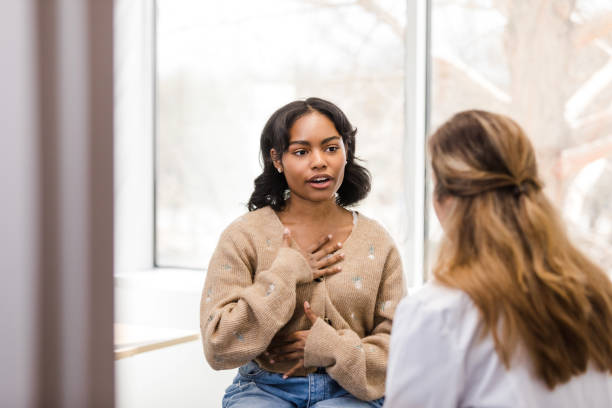 University student motions towards her chest as she describes the discomfort she has been experiencing stock photo