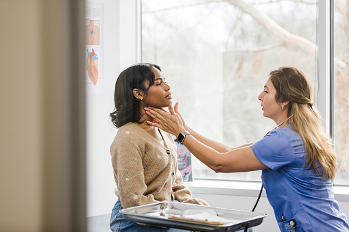 The mature adult doctor gently touches the young woman's throat as she checks for swollen lymph nodes.