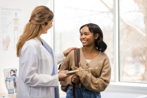 Female doctor smiles and congratulates female college student The mid adult female doctor congratulates the young adult female university student about the good news. girl patient stock pictures, royalty-free photos & images