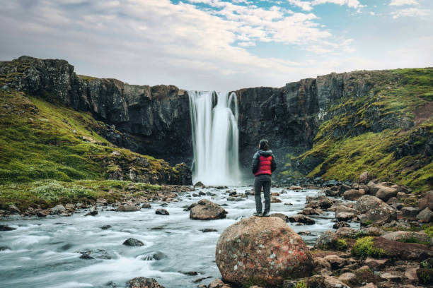 cascata di gufufoss che scorre con donna turistica asiatica in piedi sulla roccia a seydisfjordur, a est dell'islanda - flowing rock national park waterfall foto e immagini stock