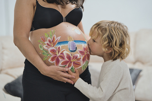 Close-up of the son kissing his mother's pregnant belly. The mother has a drawing on her belly.