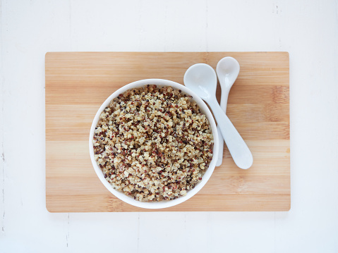 White and red cooked quinoa in a bowl. Flat lay on bamboo board beside white spoons.
