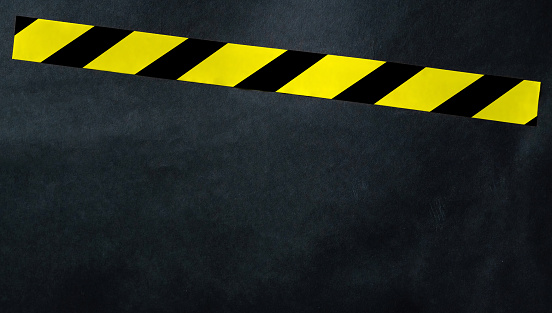 Yellow tape with black and yellow stripes on a dark background. Warning ribbon.