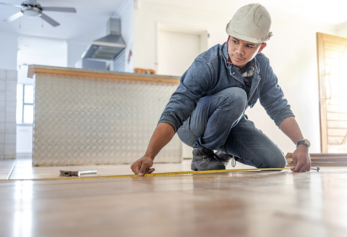 Man, carpenter and measure floor with tape, home interior and buildings maintenance. Builder, construction and handyman measuring flooring on ground, wood board house and property renovation tools