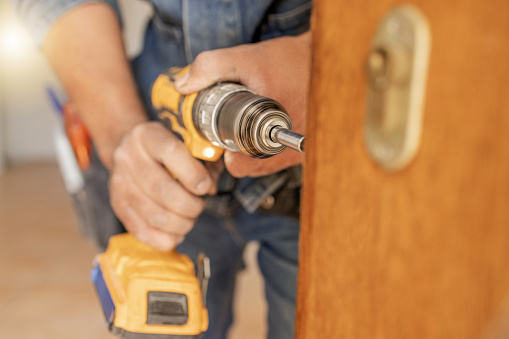 Locksmith, maintenance and handyman with drill, home renovation and fixing, change door locks with power tools. Construction, building industry and trade with manual labour, vocation and employee