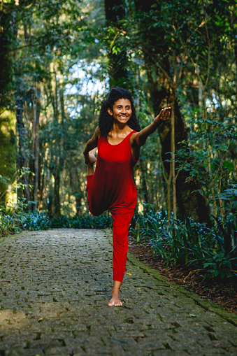 portrait of black brazilian woman, wearing a red jumpsuit, in yoga pose outdoors