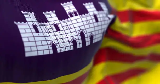 Close-up of the Balearic Islands flag waving in the wind. Four red lines on yellow with white castle on purple canton. 3D illustration render. Selective focus. Close-up. Rippled Textile