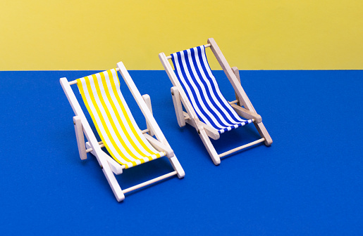 Two sun loungers, two beach chairs, couple, two hammocks with white and yellow and white and blue stripes on a solid blue and yellow background. isolated background.  Close up view. 3d object. Summer vacation concept, relax in summer, beach, sunbath, minimalism, swimming pool, vacation, sun destination, disconnect in summer.