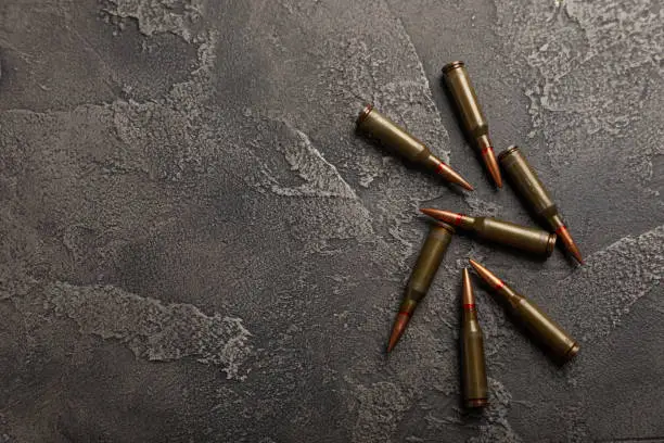 Photo of Bullets and ammo magazine on black textured marble. Bullets of a kolashnikov assault rifle close-up with space for text. Cartridges for a rifle and a carbine on a wooden background. Military concept.