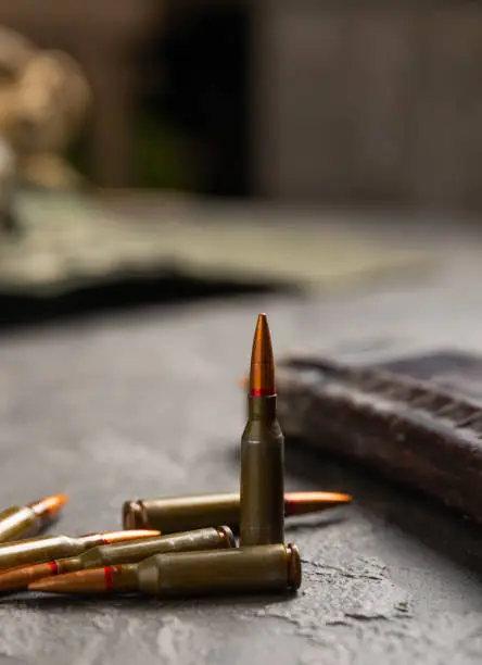 Photo of Bullets and ammo magazine on black textured marble. Bullets of a kolashnikov assault rifle close-up with space for text. Cartridges for a rifle and a carbine on a wooden background. Military concept.